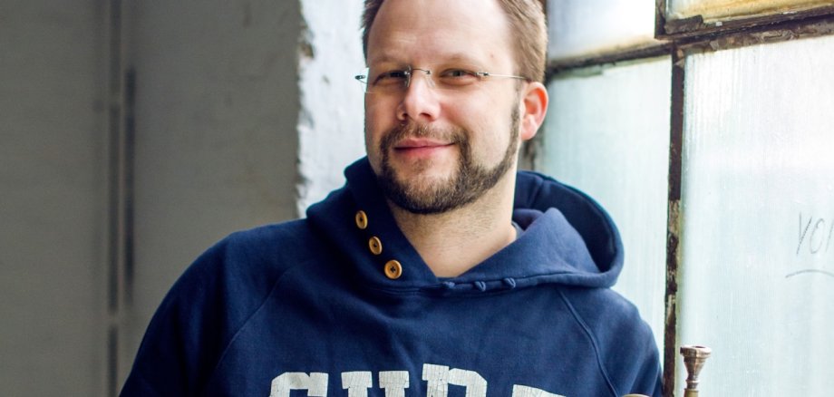 Ein Mann im blauen Pullover hält eine Trompete in der Hand.