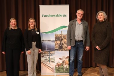 Vier Personen stehen auf einer Bühne. In der Mitte von ihnen ist ein RollUp des Westerwaldkreises.