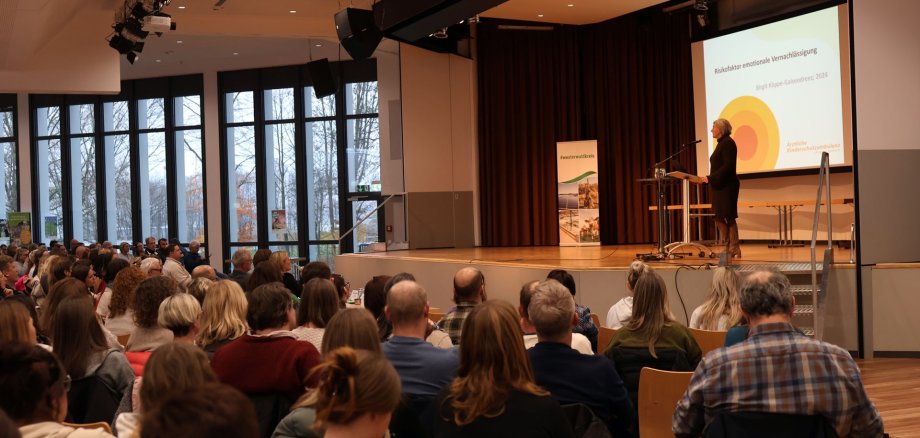 Auf der Bühne steht die Referentin vor vollbesetzten Stuhlreihen.