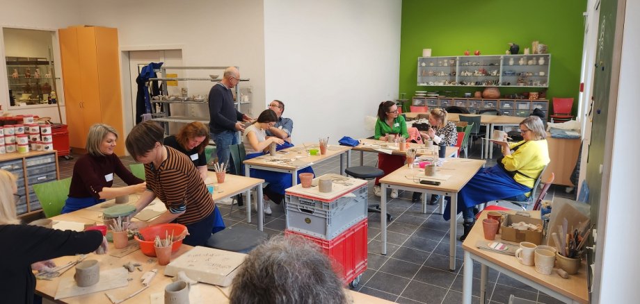 In der Keramikwerkstatt arbeiten Frauen und Männer an Tischen mit Ton.