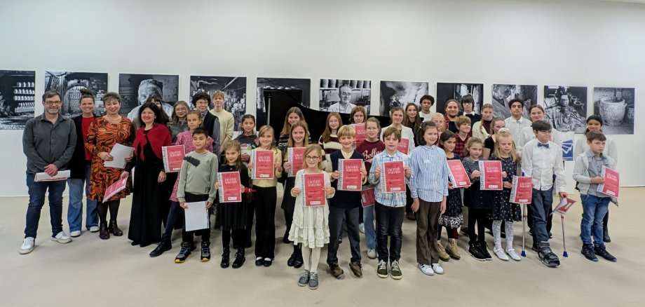 Viele Jungen und Mädchen stehen gemeinsam mit einigen Erwachsenen im Keramikmuseum vor einer Wand mit Schwarz-Weiß-Bildern und halten rote Urkunden in der Hand.