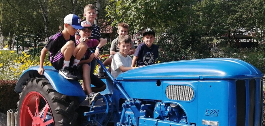 Mehrere Kinder sitzen auf einem großen blauen Traktor