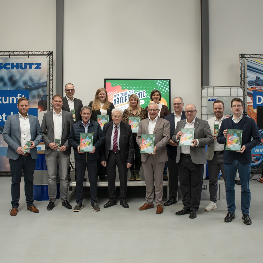 Eine große Gruppe Menschen steht mit Ausgaben der Ausbildungsfibeln in der Hand in einem Raum.