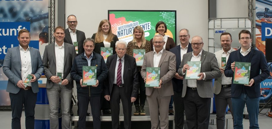 Eine große Gruppe Menschen steht mit Ausgaben der Ausbildungsfibeln in der Hand in einem Raum.