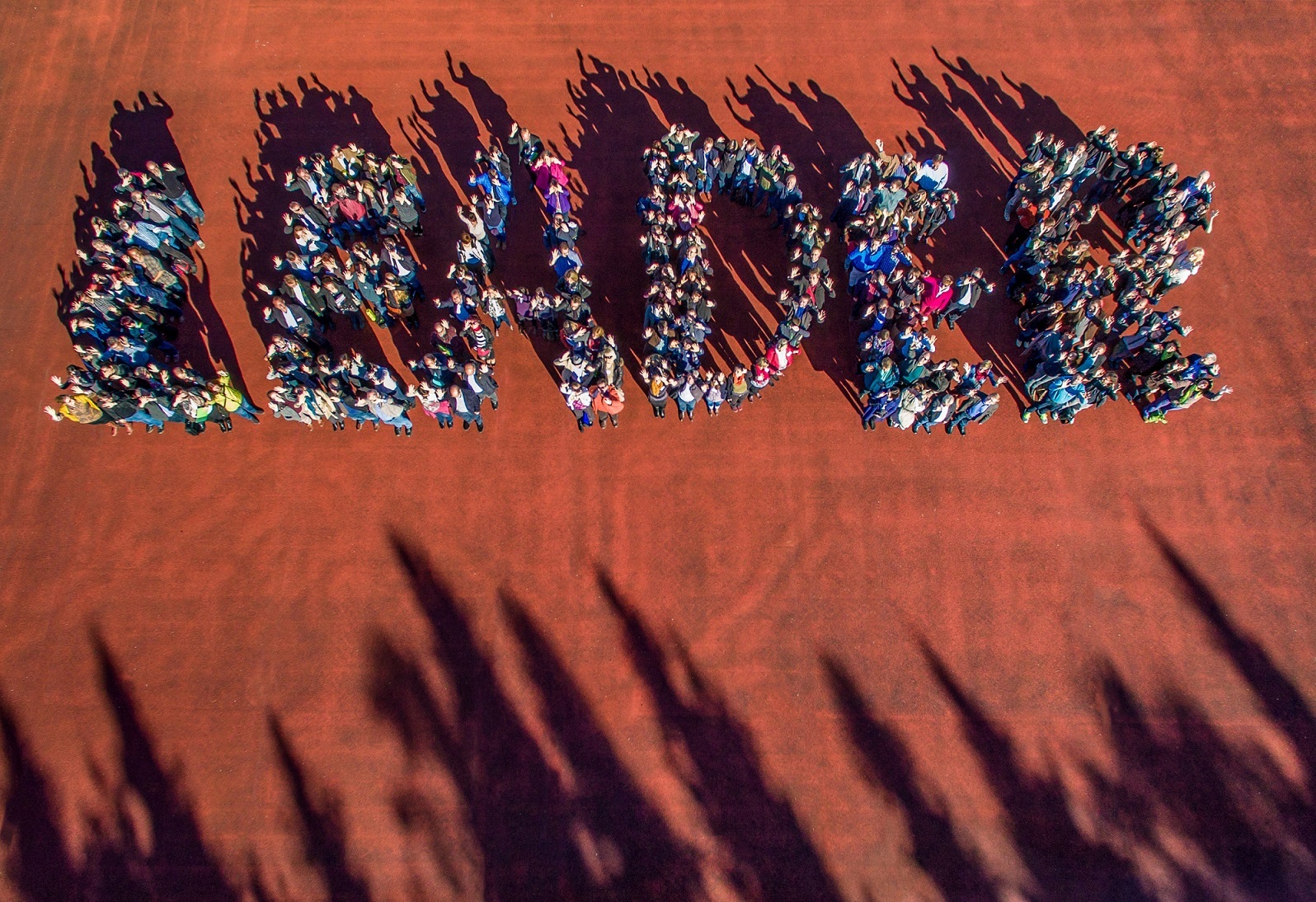 Eine große Gruppe Menschen steht zusammen und formt von oben fotografiert den Schriftzug "Leader"