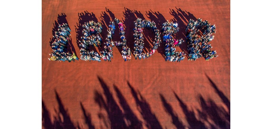 Eine große Gruppe Menschen steht zusammen und formt  von oben fotografiert den Schriftzug "Leader"