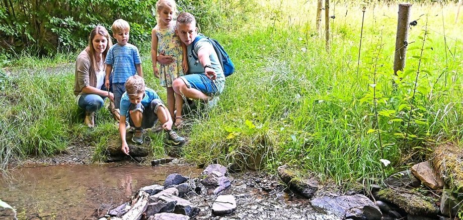 Kinder verschiedenen Alters stehen an einem Bachlauf.