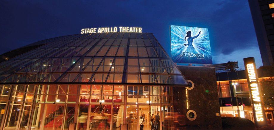 Das Stage Apollo Theater bei Nacht ist ein hell erleuchteter Glasbau, rechts mit dem Werbeplakat für das Musical "Die Eiskönigin".