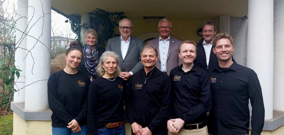 Mehrere Frauen und Männer stehen vor einem Gebäude mit großen Säulen links und rechts.