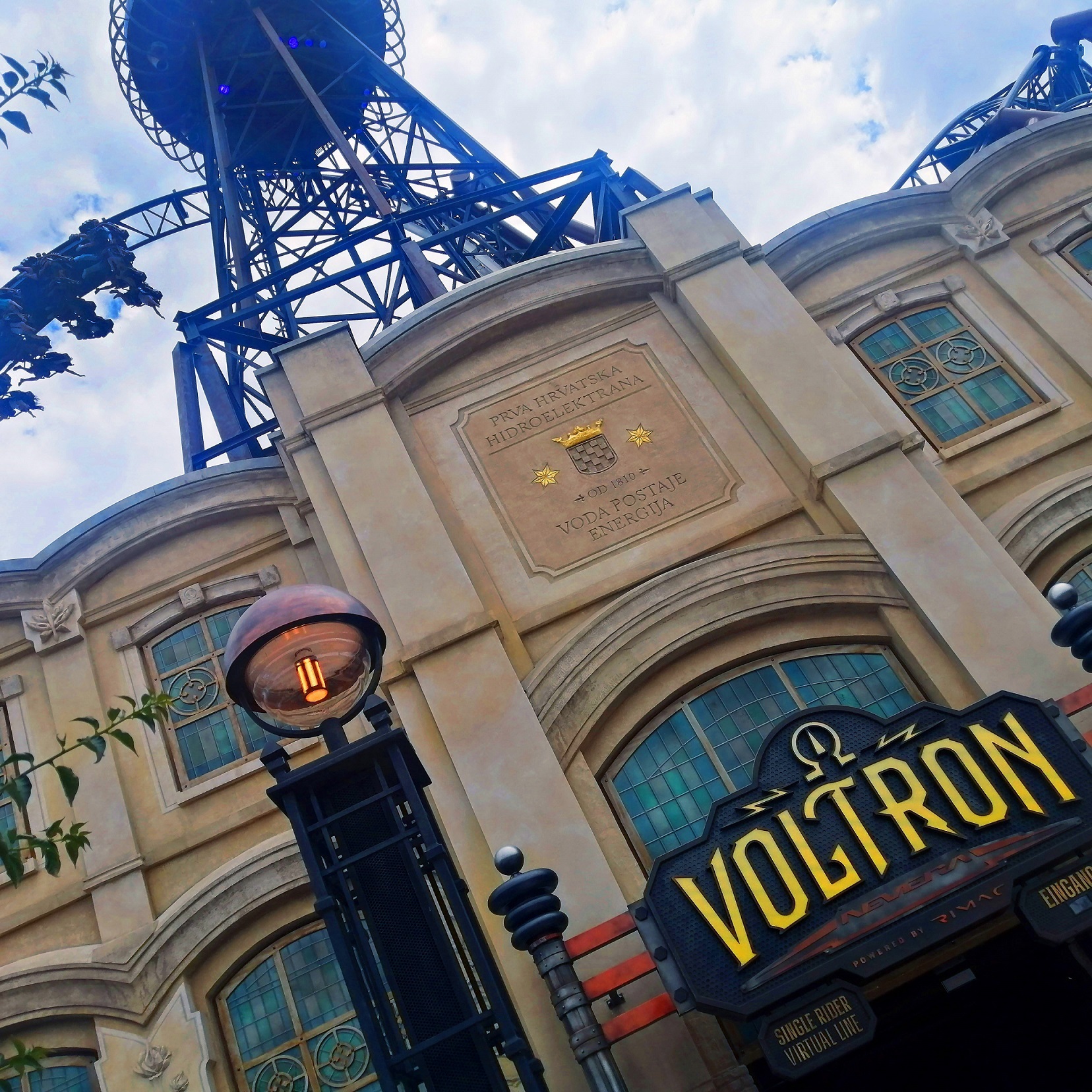 Über einem Gebäude mit der Aufschrift Voltron erhebt sich der Looping einer Achterbahn mit Passagieren.