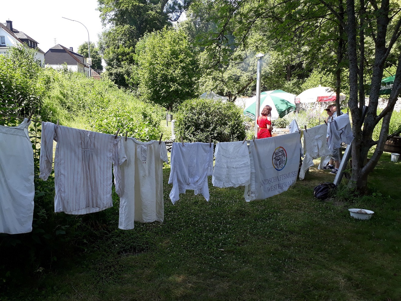 Auf einer Wäscheleine im Garten hängen große, historisch anmutende weiße Kleiderstücke.