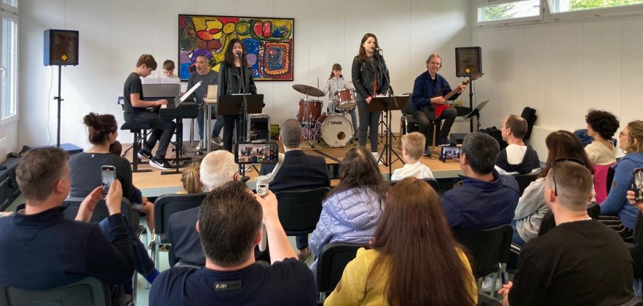 Auf einer Bühne musizieren Schülerinnen und Schüler mit verschiedenen Instrumenten vor einem Publikum.