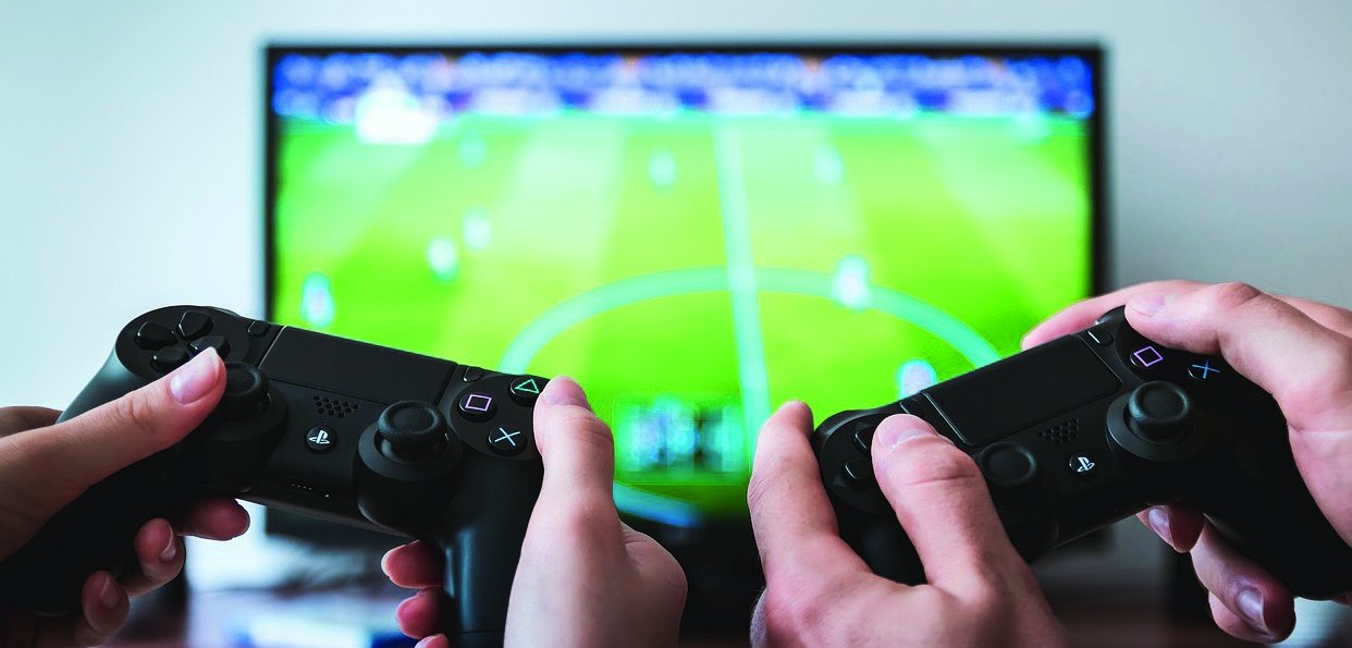 Zwei Jugendliche zocken mit Gamecontrollern vor einem Bildschirm.