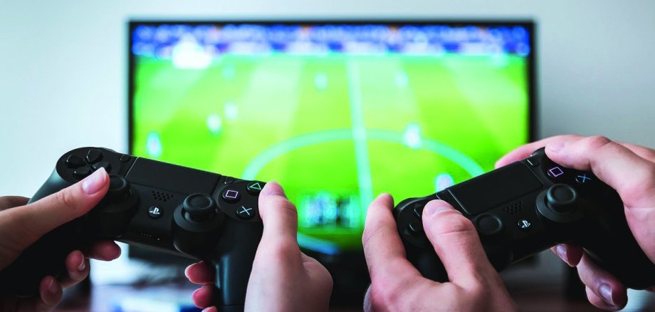 Zwei Jugendliche zocken mit Gamecontrollern vor einem Bildschirm.
