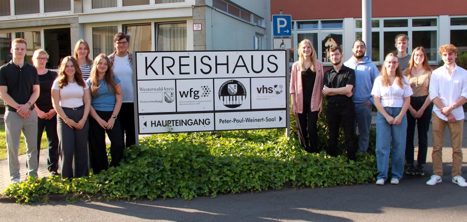 Die Nachwuchskräfte von 2024 haben sich um das Eingangsschild der Kreisverwaltung aufgestellt.