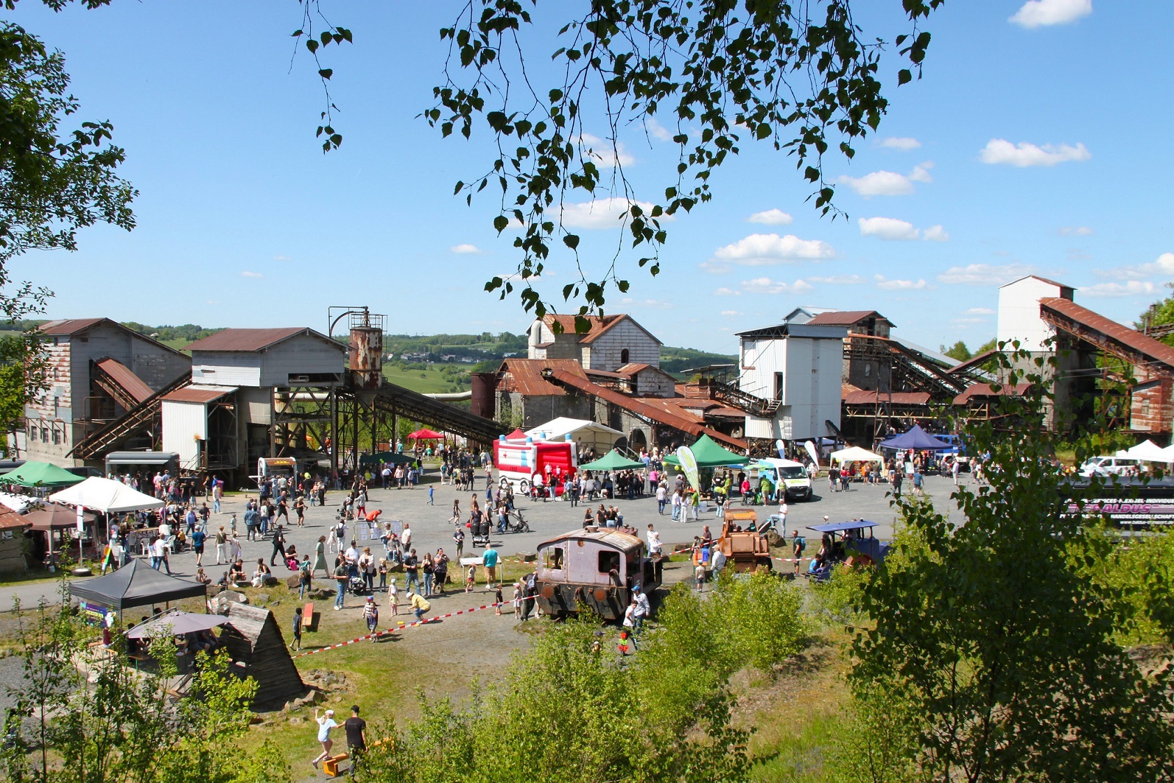 Von einem Hügel aus ist das Gelände des Parks mit seinen Industrieanlagen, dazwischen Hüpfburgen und Besucher sichtbar.