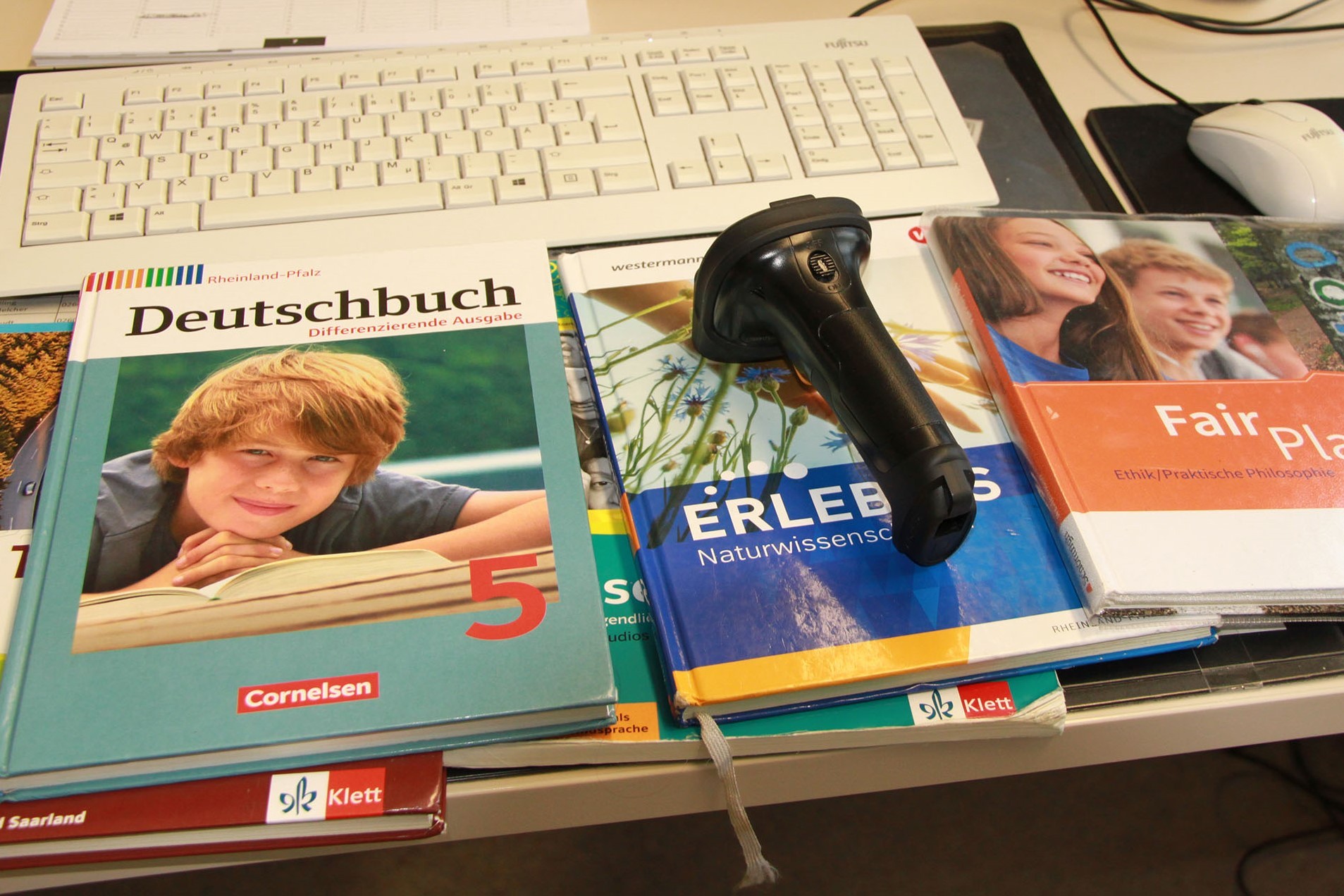 Auf einem Schreibtisch liegen mehrere gebrauchte Schulbücher und ein Handscanner.