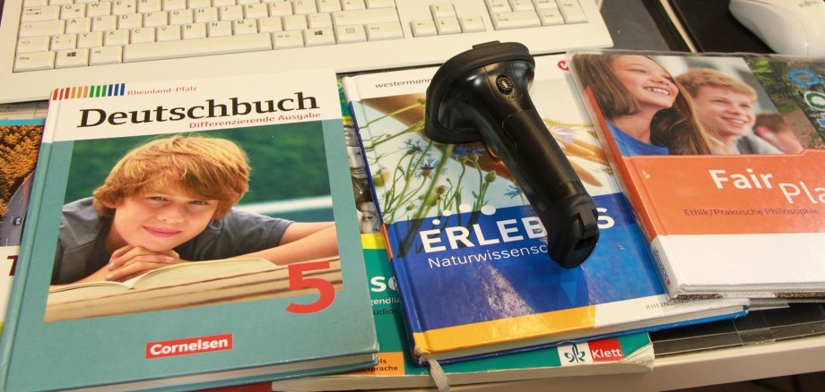 Auf einem Schreibtisch liegen mehrere gebrauchte Schulbücher und ein Handscanner.
