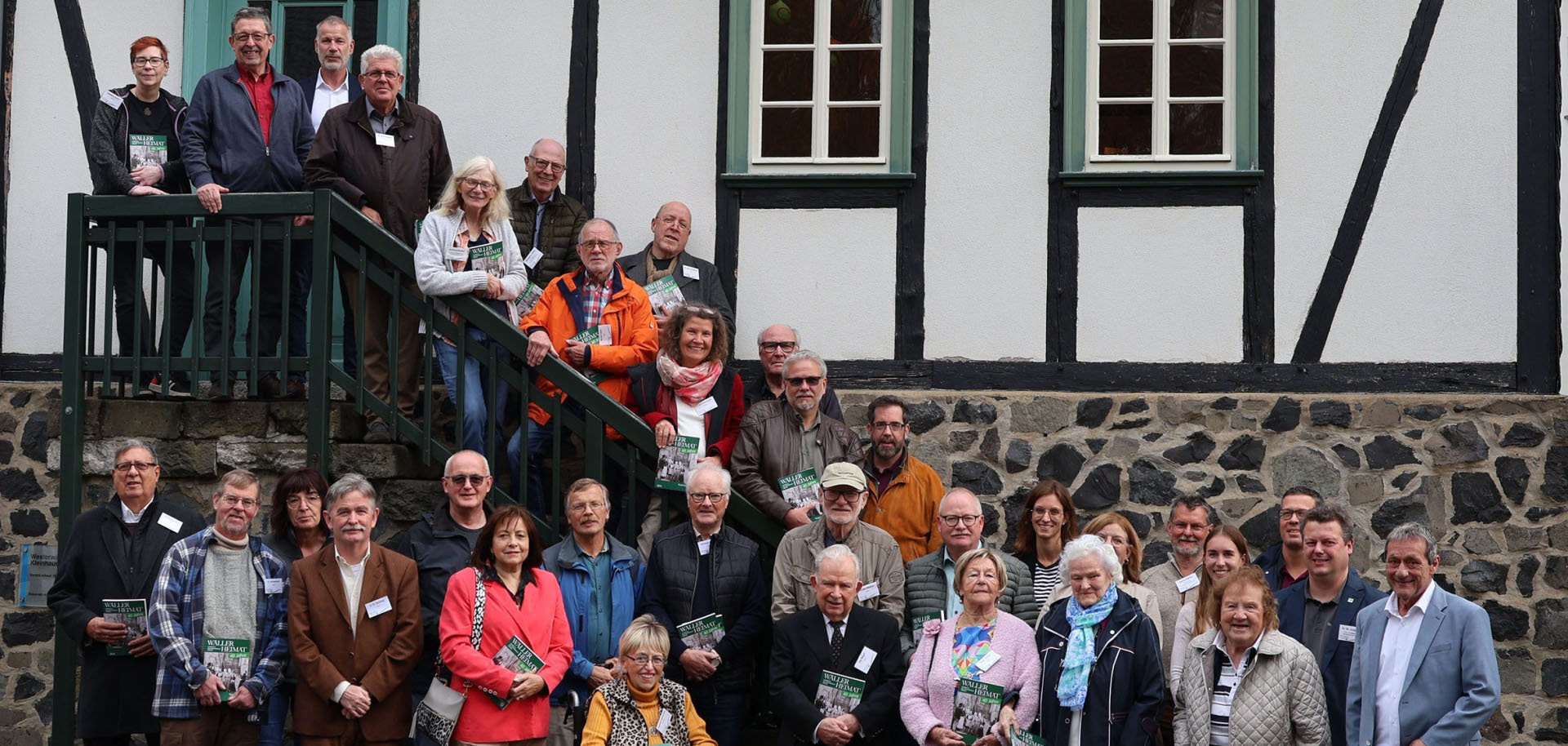 Vor einem Fachwerkhaus mit Treppe steht eine große Gruppe Menschen.