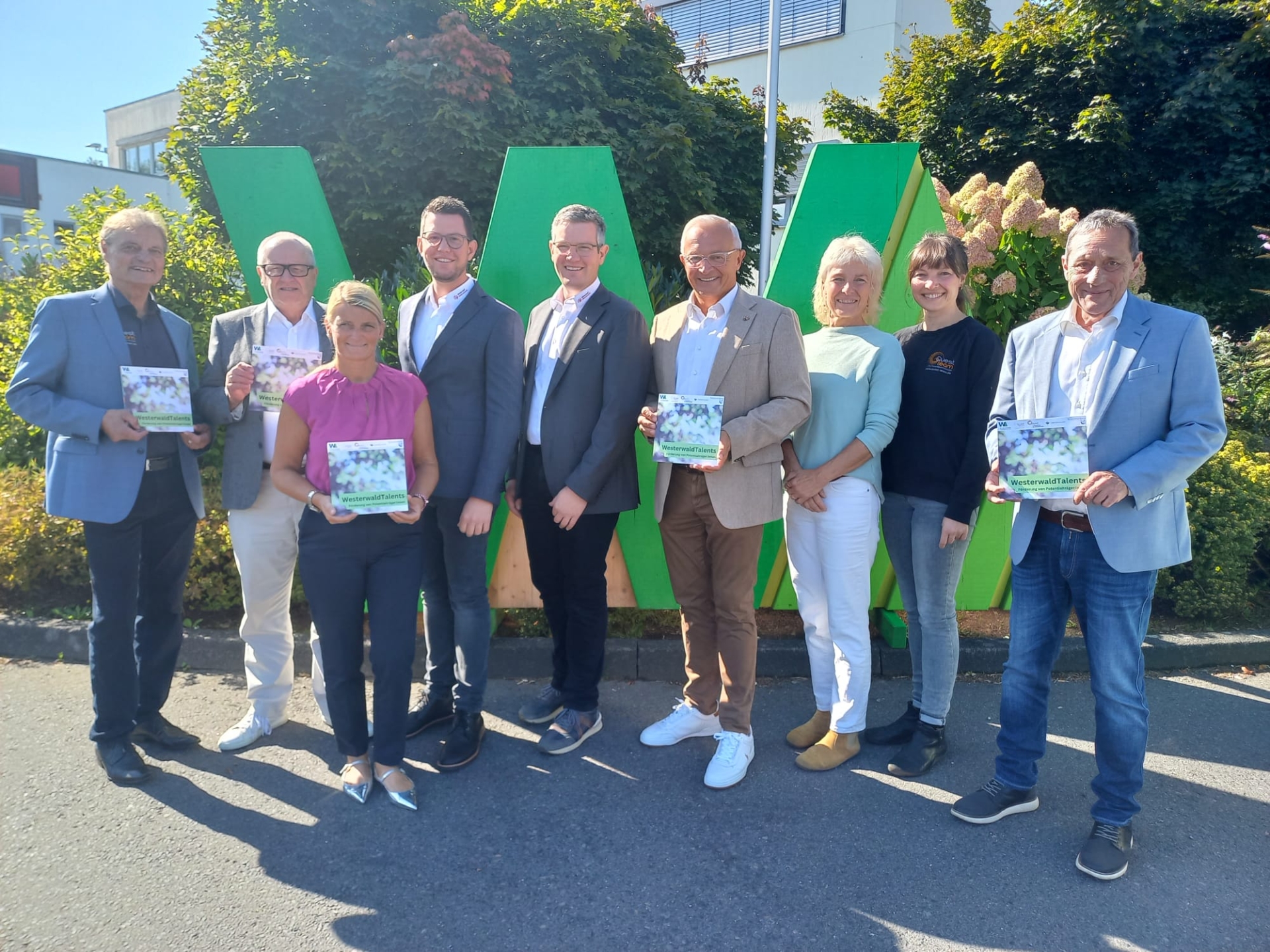 Mehrere Frauen und Männer stehen vor einem großen grünen W mit einem Flyer von WesterwaldTalents in der Hand.