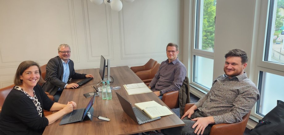 Eine Frau und drei Männer sitzen mit Laptops rundherum um einen Tisch