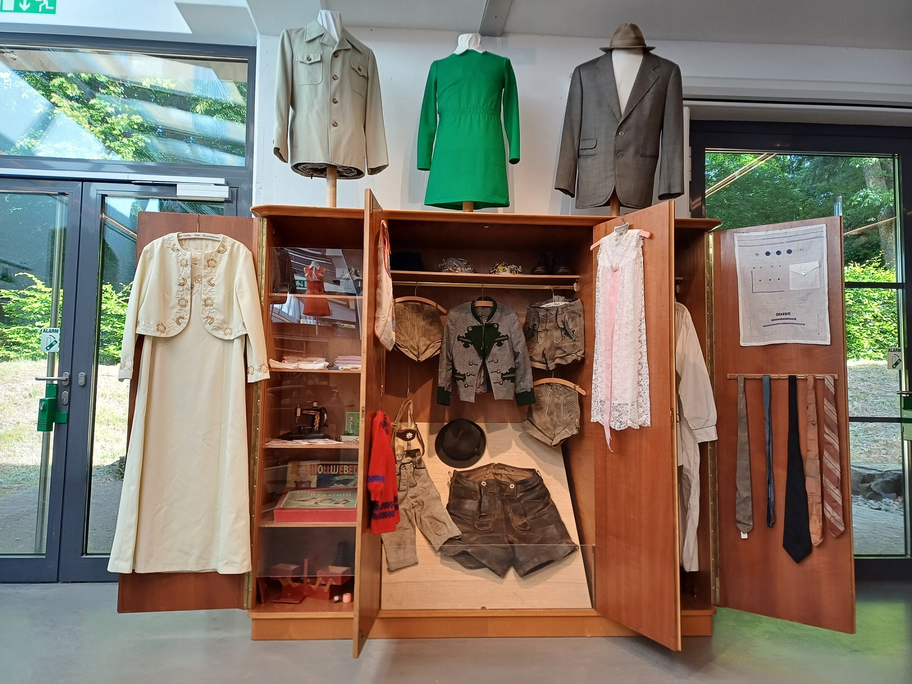 In einem alten geöffneten Kleiderschrank hängen mehrere alte Kleidungsstücke, darunter Kleider, Jacketts und Blusen.