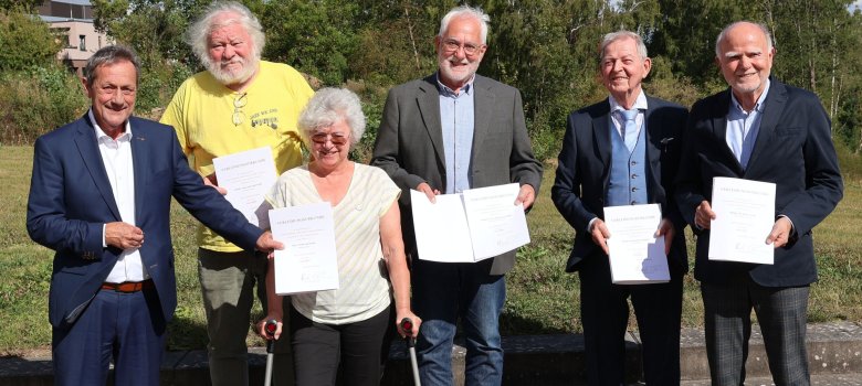 Eine Gruppe von Menschen steht im Freien mit Urkunden in der Hand.