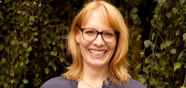 Eine blonde Frau hält einen Stapel Bücher in den Händen.