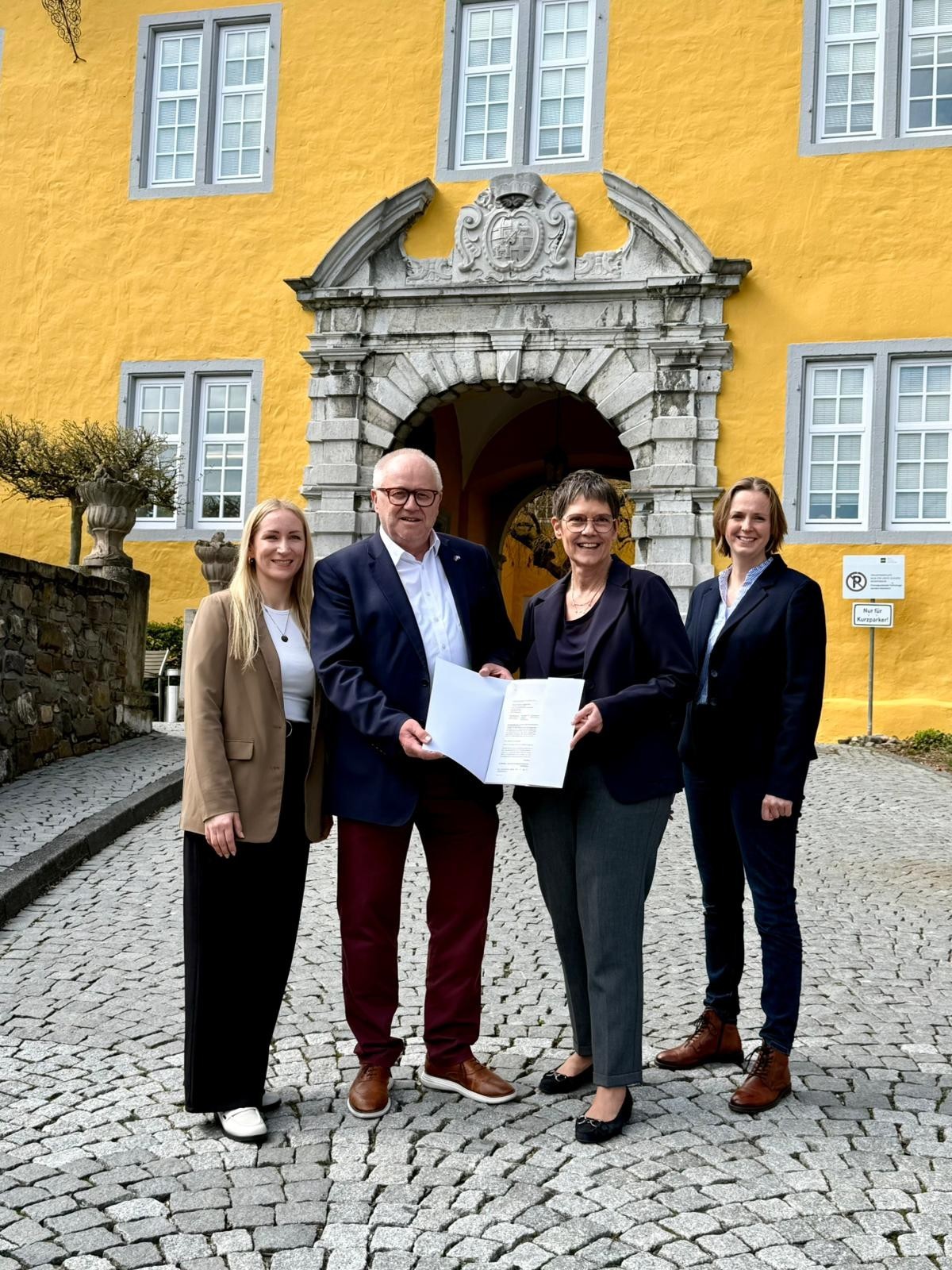 Drei Frauen und zwei Männer stehen mit einer Urkunde vorm Schloss in Montabaur.