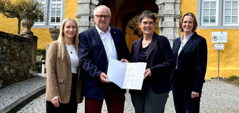 Drei Frauen und zwei Männer stehen mit einer Urkunde vorm Schloss in Montabaur.