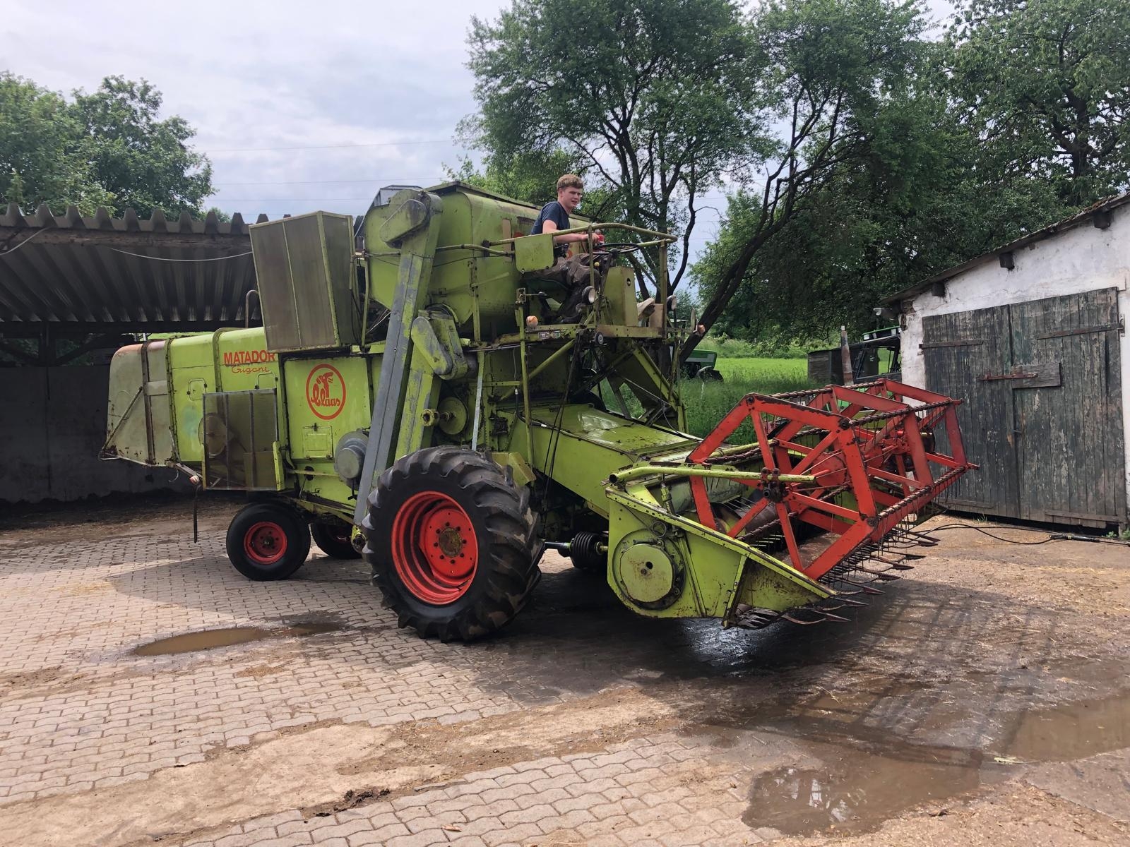 Ein grüner Mähdrescher mit rotem Mähwerk steht auf einem gepflasterten Hof.
