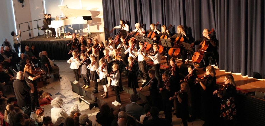 Auf einer Bühne sitzen Musiker mit Streichinstrumenten.