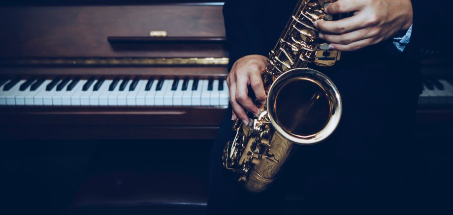 Vor einem Klavier spielen Hände auf einem Saxophon.