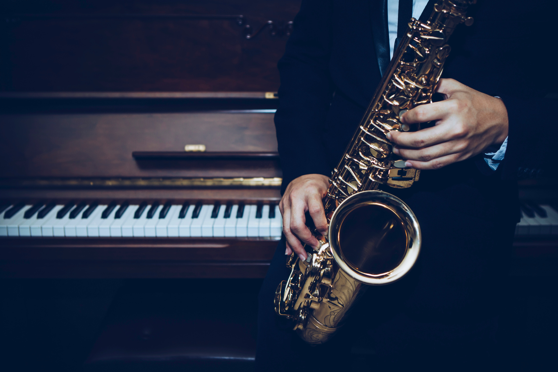 Vor einem Klavier spielen Hände auf einem Saxophon.