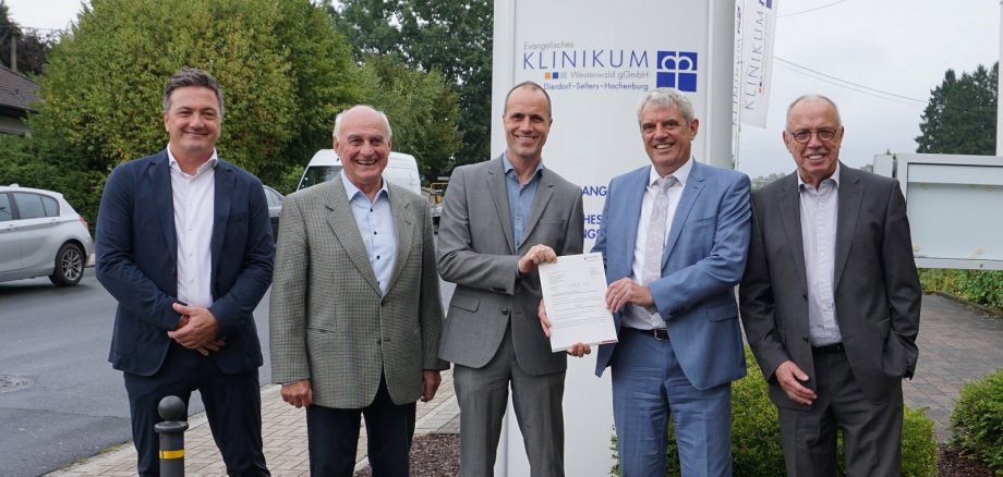 Männer mit einer Urkunde stehen vorm Klinikum-Schild.