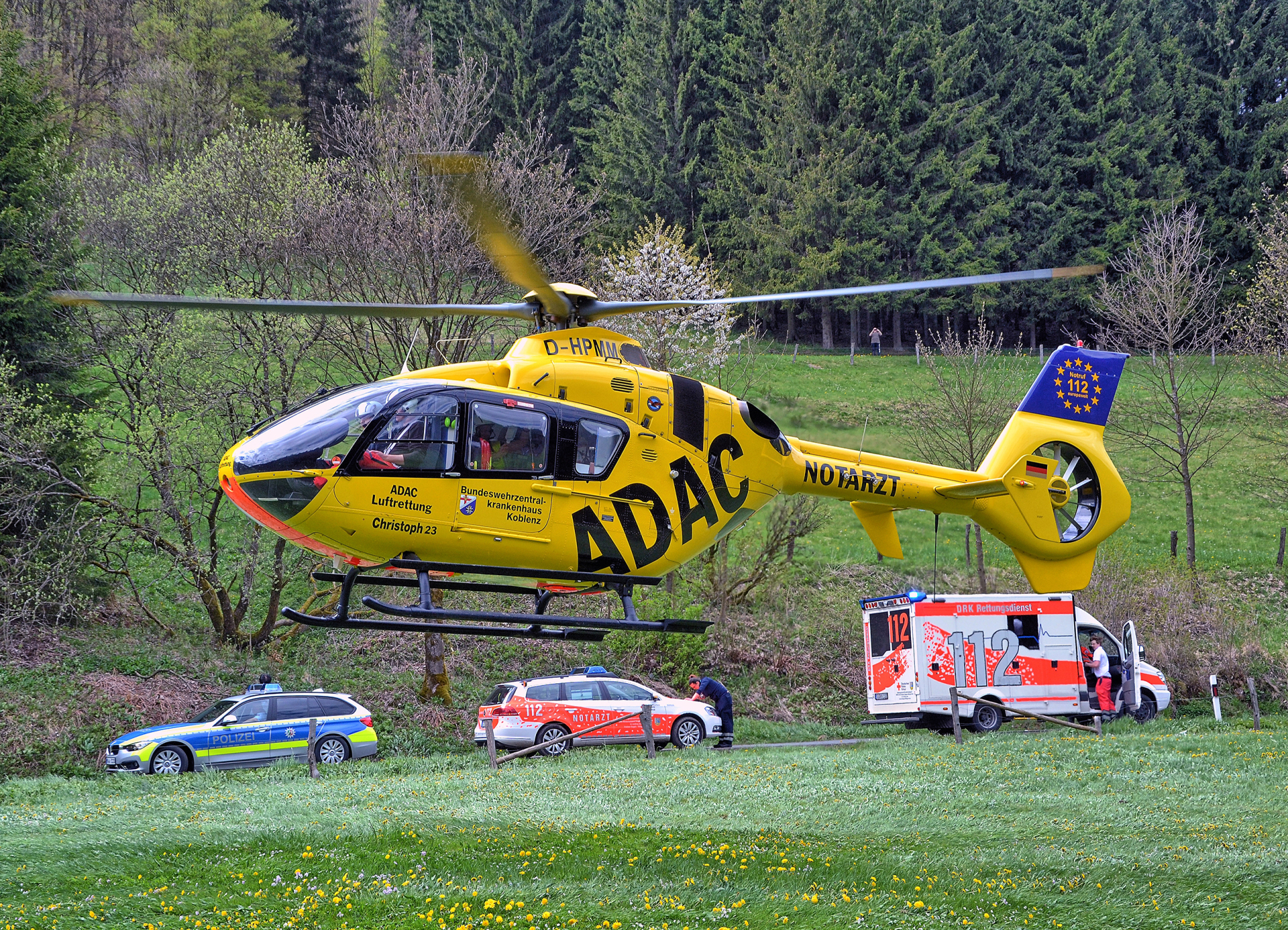 Ein Rettungshubschrauber landet auf einer Wiese vor Rettungs- und Polizeiwagen.