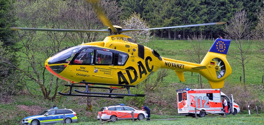 Ein Rettungshubschrauber landet auf einer Wiese vor Rettungs- und Polizeiwagen.