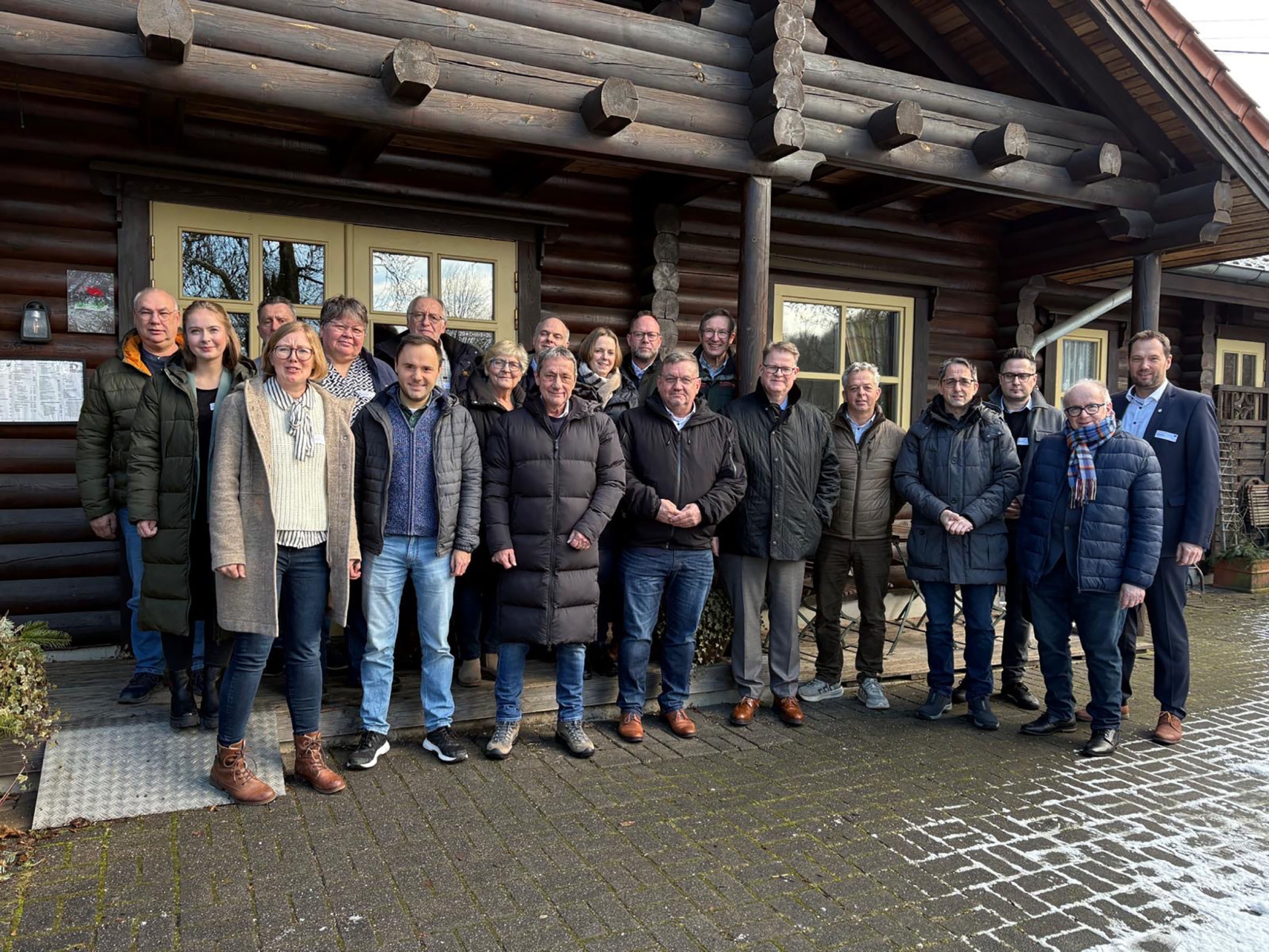 Eine Gruppe von Menschen steht vor einem Holzhaus.