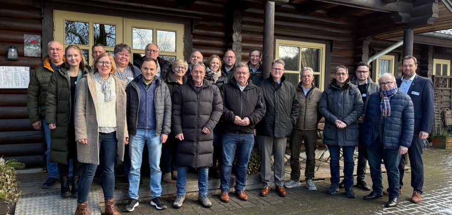Eine Gruppe von Menschen steht vor einem Holzhaus.