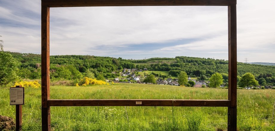Ein großer Holzrahmen steht am Weg und bildet ein Fotomotiv für einen idyllischen Wäller Ort.