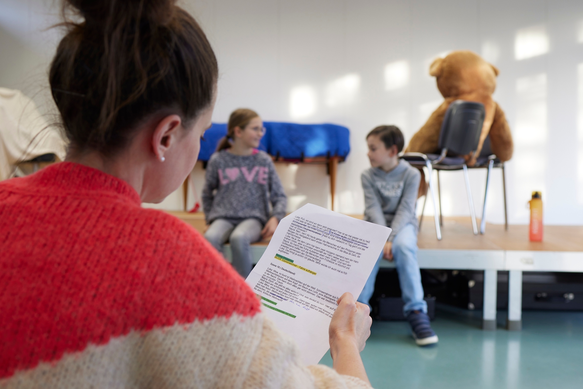 Eine Frau mit Textblatt übt mit zwei Kindern etwas ein.