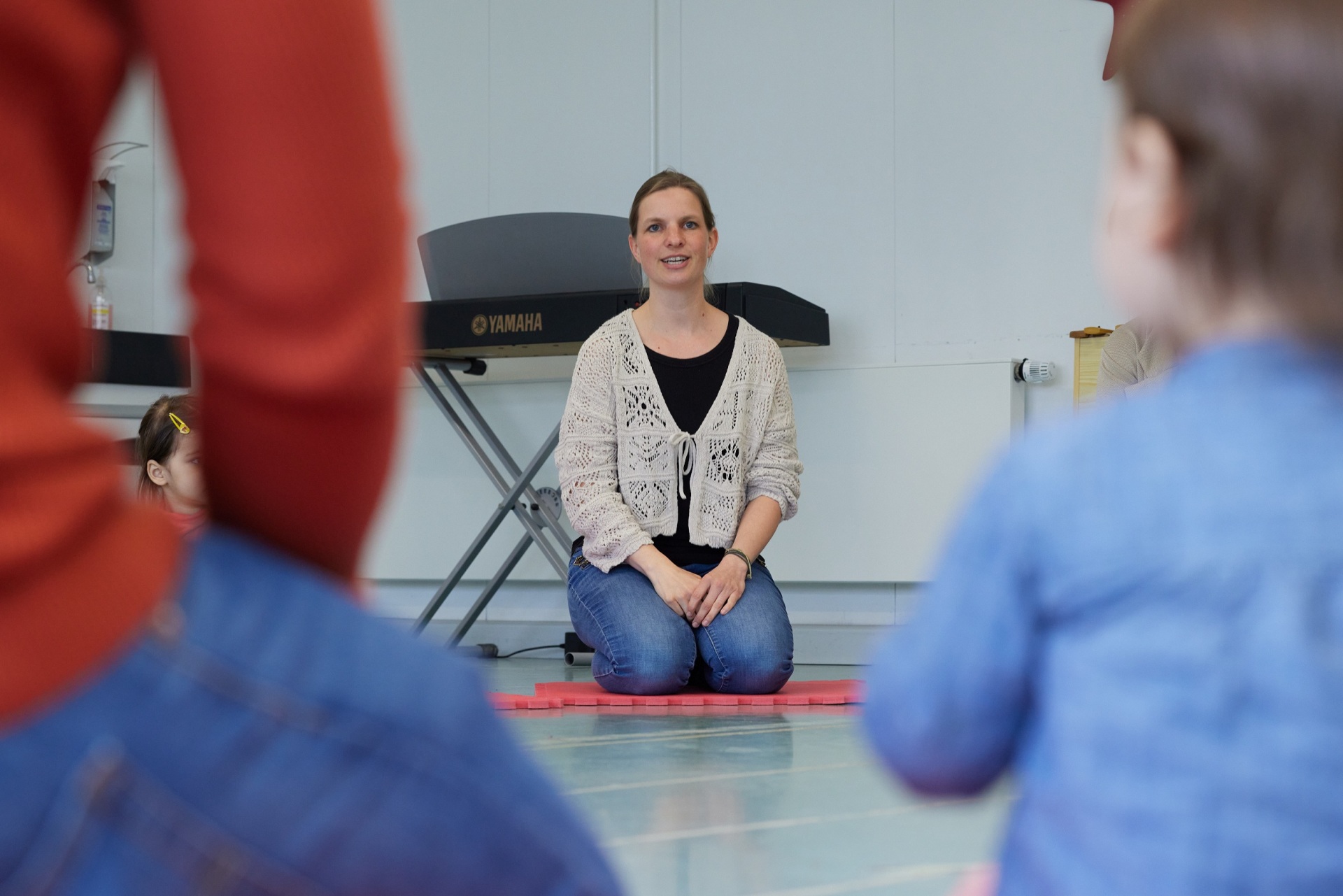 Eine Frau kniet auf einer Moosgummimatte und singt vor Kindern.
