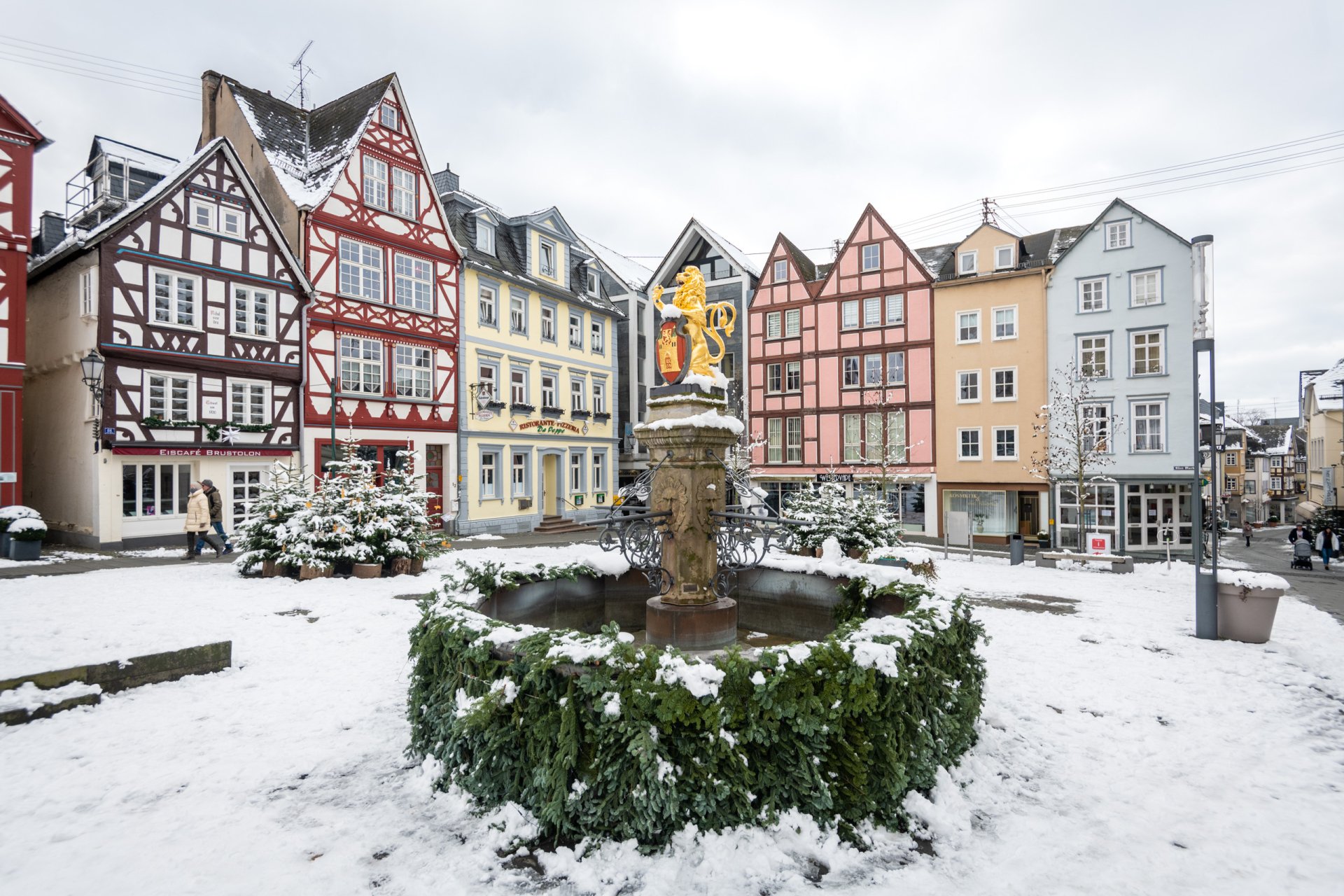 Ein mit Tannenzweigen geschmückter Brunnen im Winter vor Fachwerkhäusern.