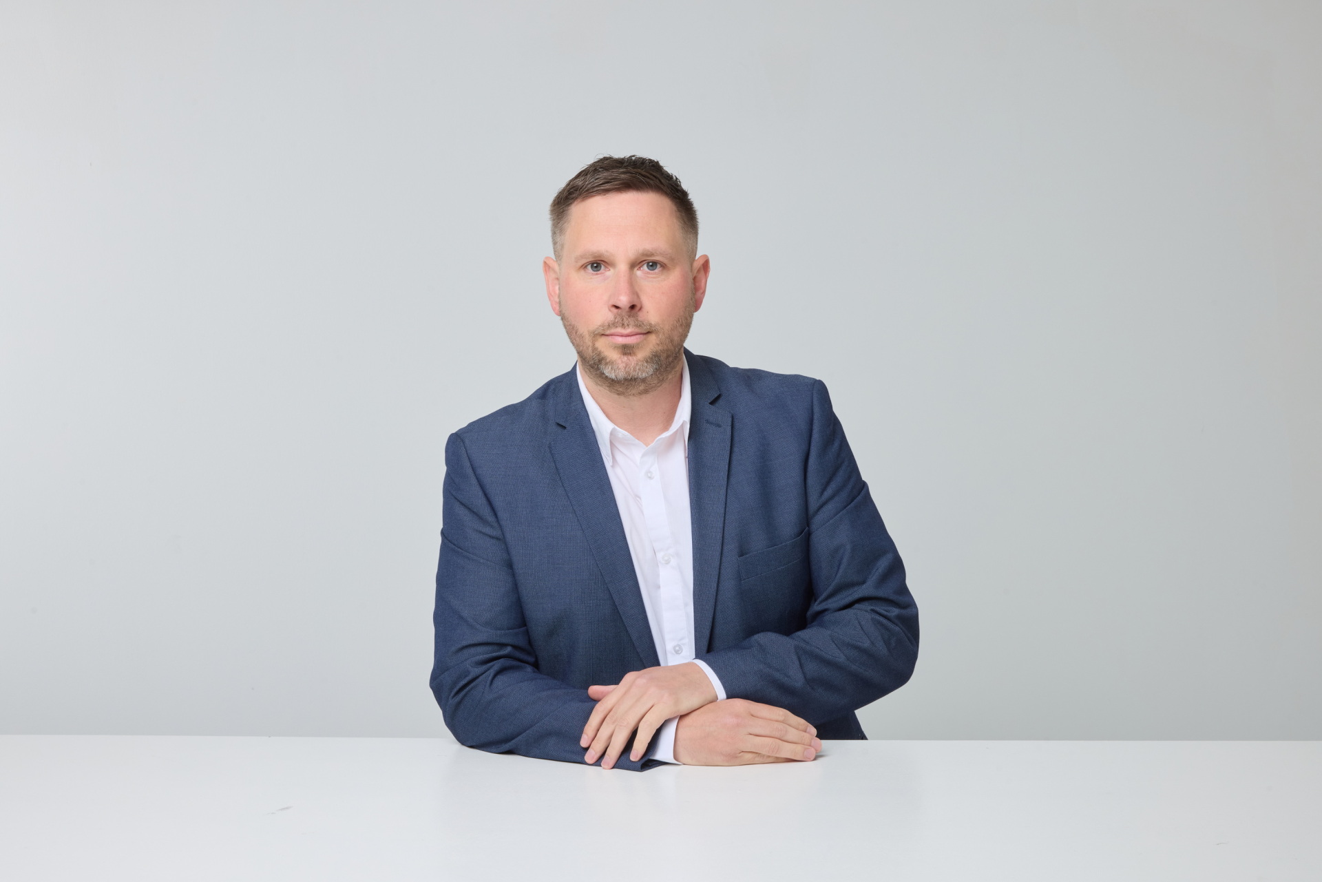 Ein Mann mit Bart und blauem Jackett lehnt an einem Tisch.
