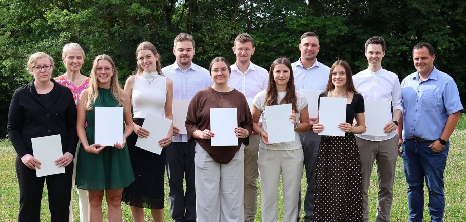 Junge Frauen und Männer stehen mit Urkunden in der Hand auf einer Wiese.