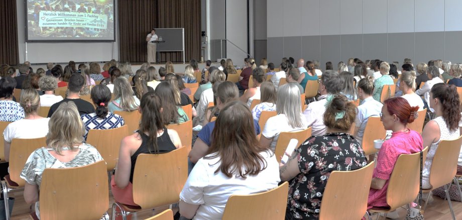 Das Publikum sitzt in Stuhlreihen vor einer Rednerin.