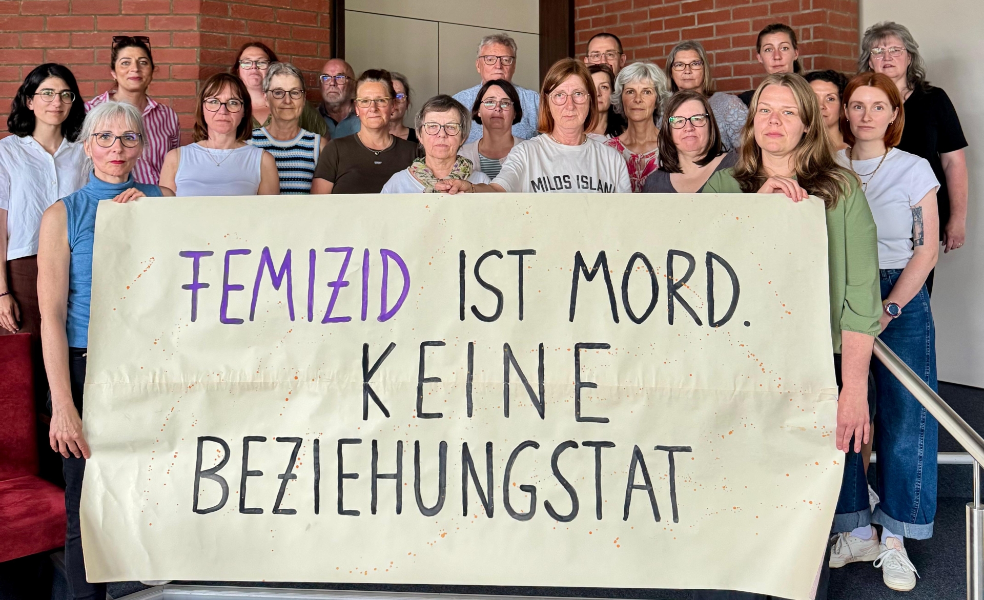 Eine Gruppe von Menschen hält ein Plakat hoch mit der Aufschrift: Femizid ist Mord keine Beziehungstat.