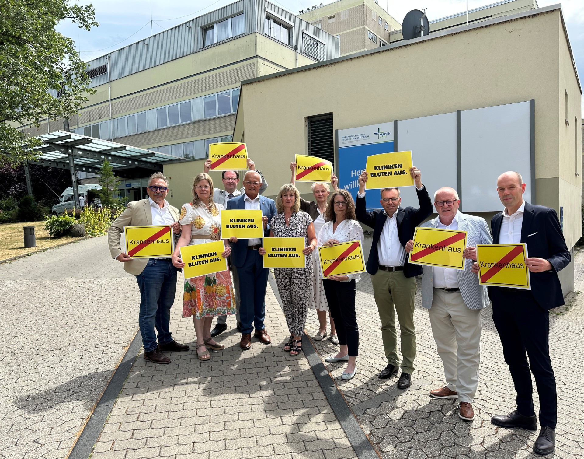 Eine Gruppe von Menschen hält vor einem Krankenhaus gelbe Schilder hoch.