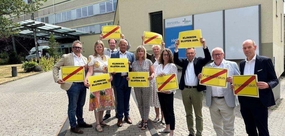 Eine Gruppe von Menschen hält vor einem Krankenhaus gelbe Schilder hoch.