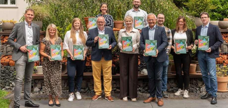 Frauen und Männer stehen mit einem Buch in der Hand vor einem Baum.